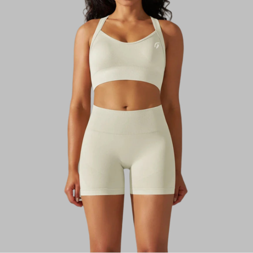 A woman wearing a ivory sports bra and shorts set on a grey background