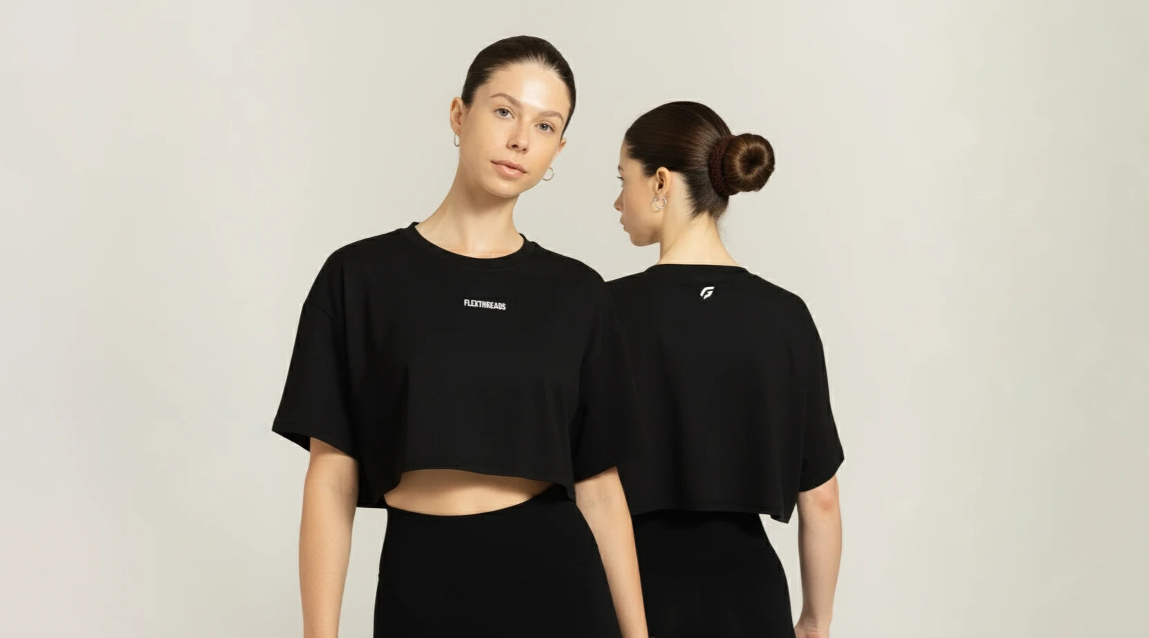 Two women wearing black t-shirts with logos on a plain background